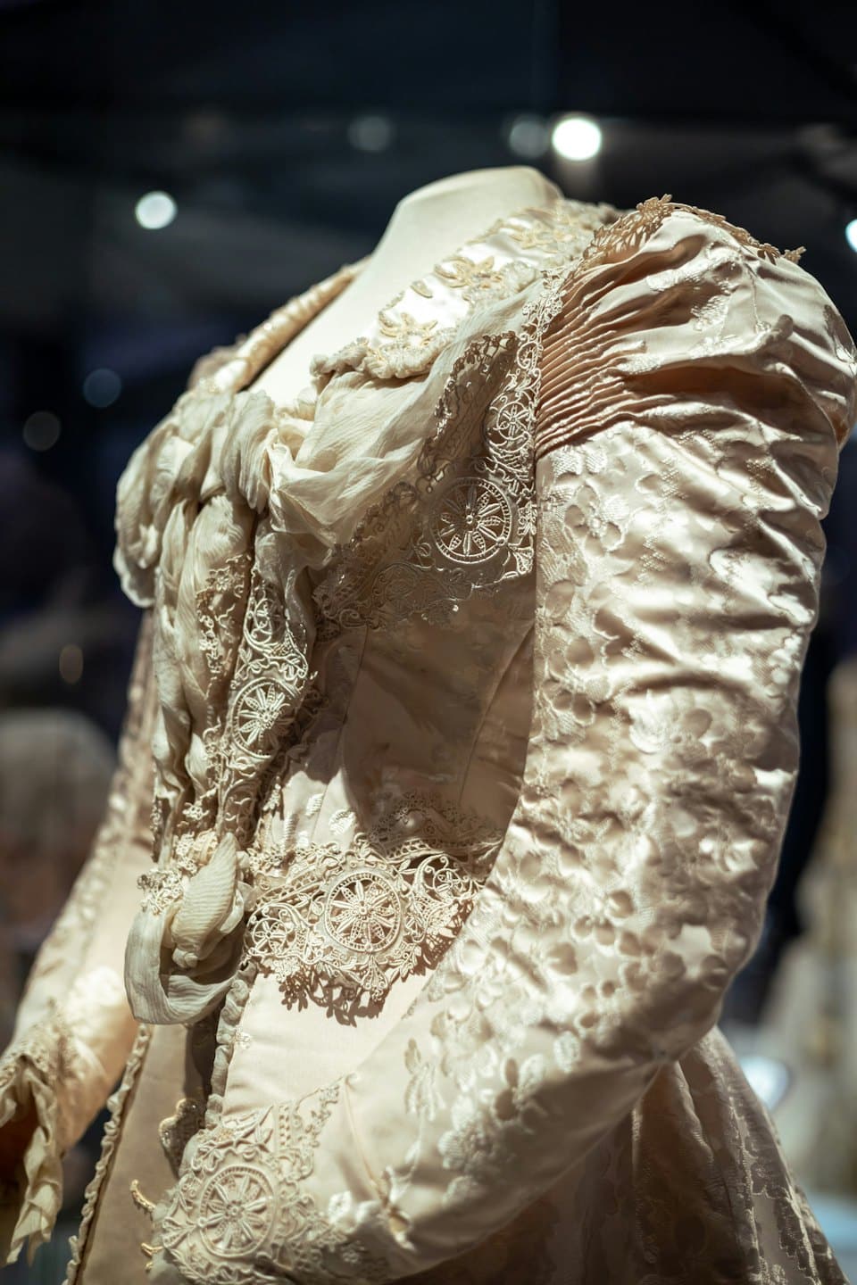 Abito antico color crema con pizzo intarsiato su un manichino.